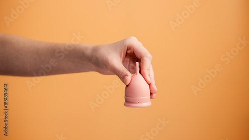 Female Hand Holding Menstrual Cup on Orange Background Minimal Hygiene