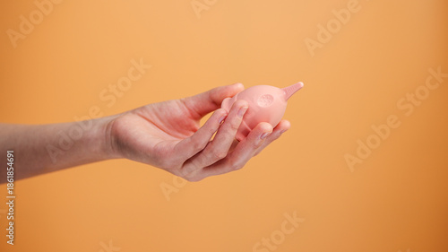Female Hand Holding Menstrual Cup on Orange Background Minimal Hygiene