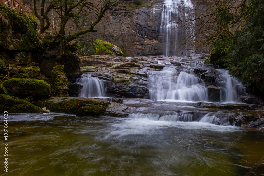Obraz premium A serene view of Suuçtu Waterfall in Bursa, with water cascading over moss-covered rocks, surrounded by lush greenery and trees, creating a peaceful, natural landscape perfect for nature lovers.