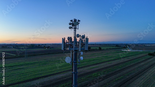 Cell tower transmitting modern telecommunication signals and 5G network connectivity over fields during a calm blue hour sunset