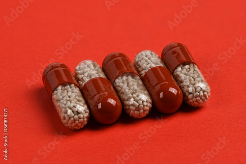 Angled Row of Red Medical Capsules with Granules on Red Background