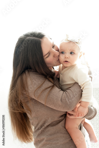 mom and baby hug and kiss on a white background of the window, a place and space for text, maternal love and care, mother and child in their arms