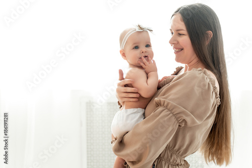 mom and baby hug and kiss on a white background of the window, a place and space for text, maternal love and care, mother and child in their arms in diapers