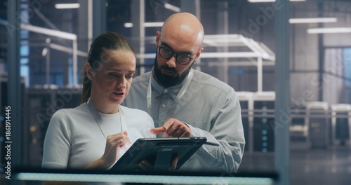 Male and Female IT Engineer Team Collaborating and Discussing Data Displayed on Digital Tablet, Standing in Secure, High Tech Environment of Data Center. Concept Teamwork and Mobile System Diagnostic.