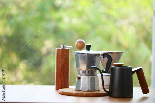 Cuadro en lienzo Coffee set with coffee grinder, jug, moka pot and brewer on wood table with green nature as background