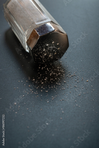 Close-Up Salt Shaker Spilling Salt Crystals On Dark Table Surface