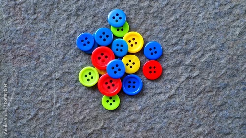 A collection of brightly colored buttons arranged in a cluster on a textured, grey surface