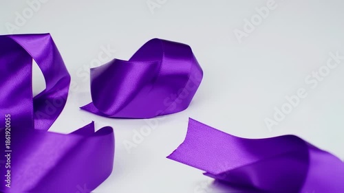 Glossy purple satin ribbon in various forms, casting shadows on a clean white surface