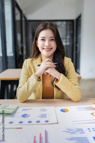 smiling Asian businesswoman with analyzing financial charts in the modern office.
