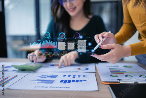Two Asian businesswoman using digital analyzing financial virtual screen in the modern office.