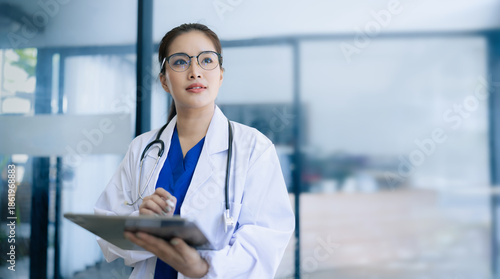 Doctor woman using digital tablet standing in clinic look at camera, Doctor woman wearing glasses and medical coat working in hospital, Healthcare professional service at modern center. 