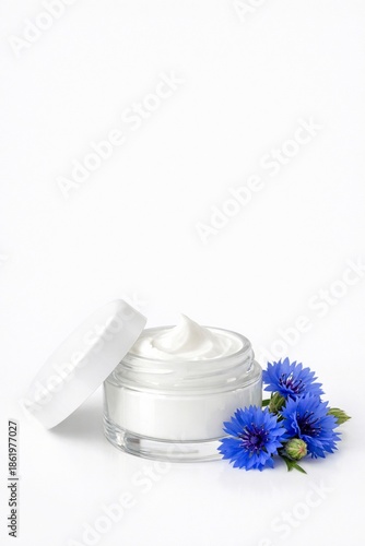 Glass jar of cream with white lid, near blue flowers. Beauty product. Remedy for face or skin around eyes with cornflower extract. Vertical banner, copy space to advertise cosmetics white background