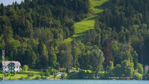 Bled, Slovenia - August 11, 2025: A panoramic view showcases the lakeside hotels and private villas of Bled, Slovenia, nestled against a steep, densely forested alpine hillside.