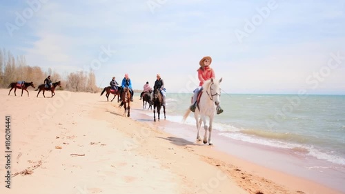 Group of people enjoying a guided horseback riding tour along a scenic beach shoreline. Riders in casual clothes follow the trail near the water. Eco-tourism, outdoor activity and natural beauty.