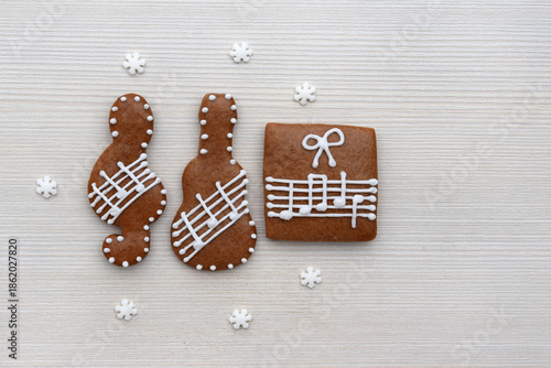 Romantic decorated gingerbread cookies in a shape of treble clef, guitar and present with notes on a staff, small snowflakes around, copy space for text