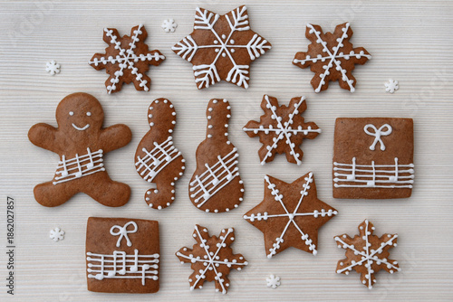 Romantic decorated gingerbread cookies in a shape of star, snowflake, present, man, treble clef and guitar with notes on a staff, small snowflakes around