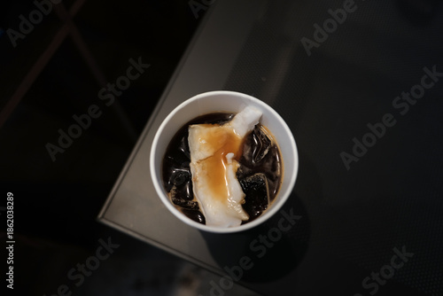 Coffee espresso with fresh coconut juice and coconut flesh in a white paper glass.