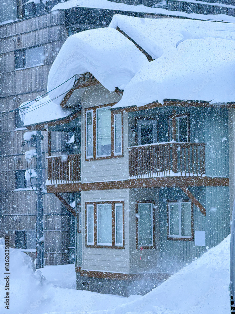 Fototapeta premium Charming wooden house stands amidst a heavy snowstorm in a ski town. The roof is laden with thick layers of snow, and large icicles hang from the edges. Magical picture of a pure winter wonderland.