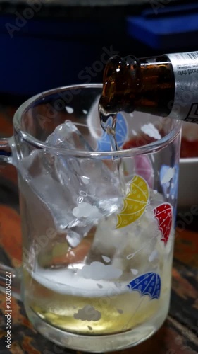 Close up of pouring cold beer into a glass filled with ice. Refreshing alcoholic beverage, summer drink concept, nightlife, party, bar, and casual drinking lifestyle.