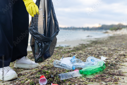 Obraz na plátně Volunteer collecting plastic waste during beach cleanup, removing litter and protecting the shoreline environment
