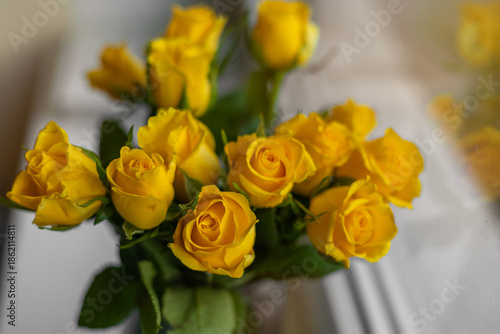 Soft-focus bouquet of vibrant yellow roses with fresh green leaves, captured indoors in natural daylight on a white windowsill.