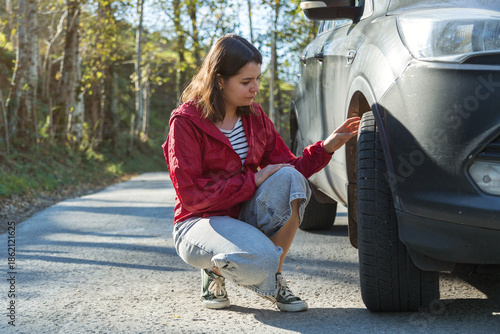 Φωτογραφία Woman checking car tire on roadside, driver inspecting wheel condition after bre