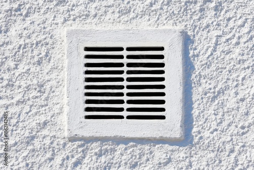 A vent set into a white wall shows the slits for air flow that help with ventilation in a home during the day