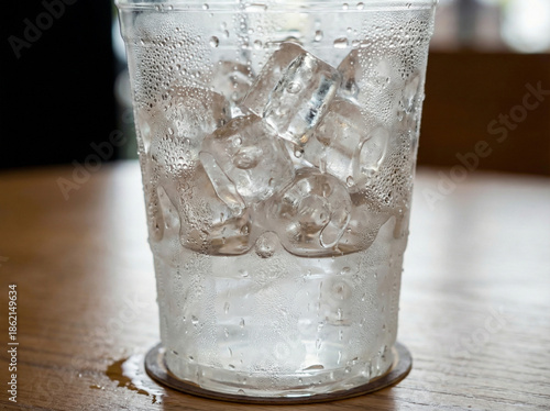 Ice cubes in clear plastic cup on wooden table 