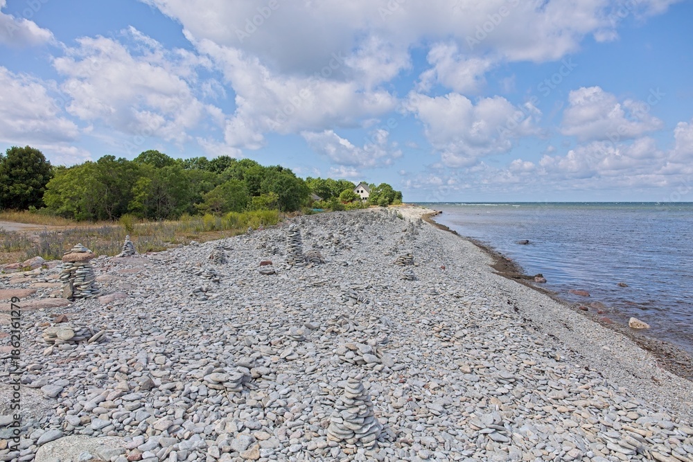 Fototapeta premium Scenic view of a shingle of pebble beach, with numerous man-made stone cairns (piles) built by visitors in summer with clouds on the sky, Tagaranna, Saaremaa, Estonia.