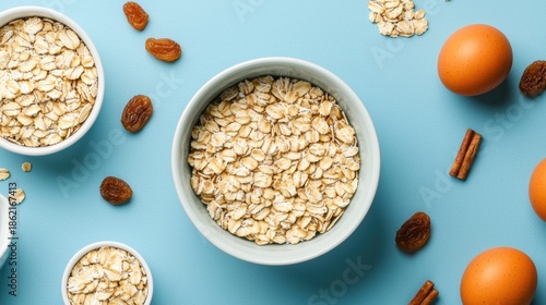 A visually appealing arrangement of oats, eggs, raisins, and cinnamon on a blue background, showcasing healthy ingredients for cooking or baking.
