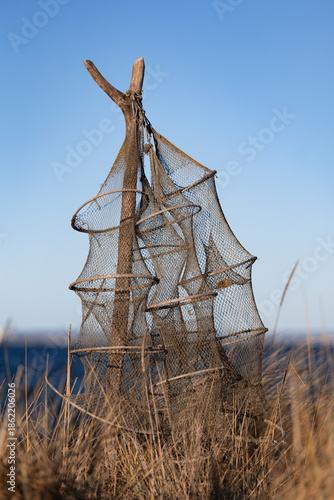 Traditionelle Reusen- bzw. Fischernetze an Holzpfählen in den Dünen am Timmendorfer Strand an der Ostsee. Die leeren Netze hängen ruhig im Wind vor blauem Himmel und vermitteln maritimes Handwerk