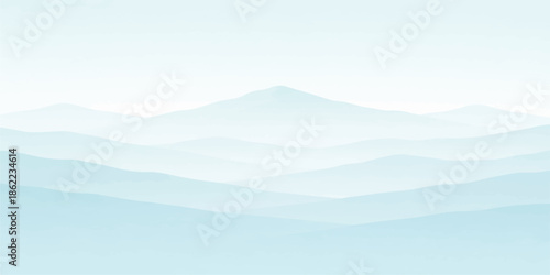 A misty mountain landscape with clouds drifting over a forest valley at sunrise as the blue sky horizon meets the hazy mountain range in the morning light