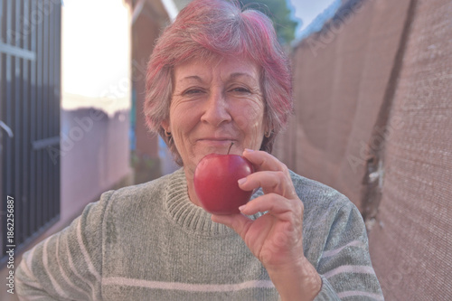 Middle-aged woman smiling confidently holding a red apple in her home