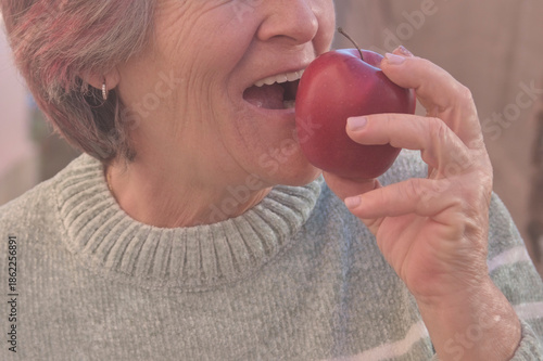 Middle-aged woman smiling confidently holding a red apple in her home