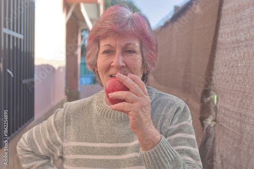 Middle-aged woman smiling confidently holding a red apple in her home