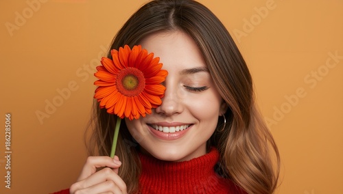 Woman Holds Orange Flower Close to Her Face While Smiling in a Soft Backgroun...