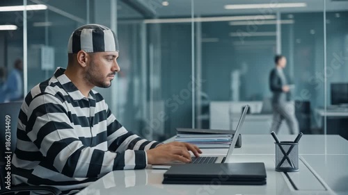 Inmate - felon prisoner inmate is working in a business office at a computer while wearing prison outfit