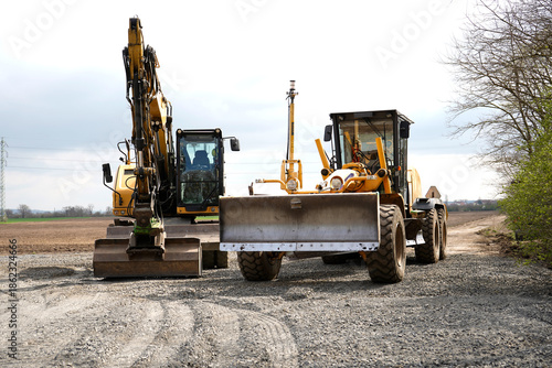 Tableau sur toile Yellow excavator and motor grader parked on a gravel construction site