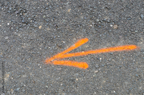 Slika na platnu Orange spray painted arrow symbol on gray asphalt road surface with gravel and s