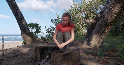 Woman roasts a sausage over a fire on the ocean shore.