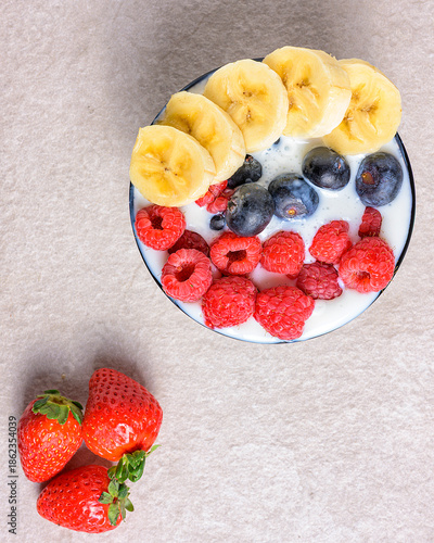 Healthy breakfast bowl with yogurt, banana, blueberries and raspberries on a stone surface