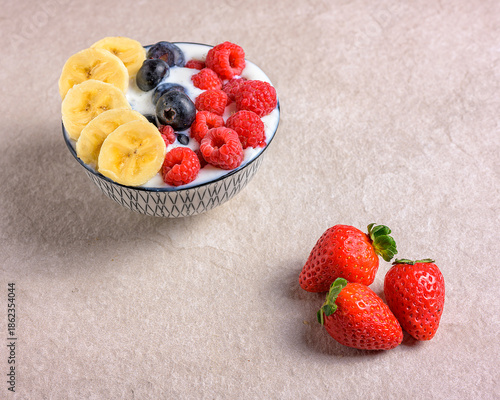 Healthy breakfast bowl with yogurt, banana, blueberries and raspberries on a stone surface
