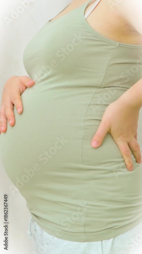 Wallpaper Mural Asian Close up of pregnant woman gently holding her belly, wearing white top and light blue pants, symbolizing care and anticipation during pregnancy and motherhood. Vertical Video. High quality 4k Torontodigital.ca