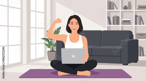 Strong smiling woman with a laptop flexes her bicep while sitting on a yoga mat in a modern living room, illustrating success and empowerment