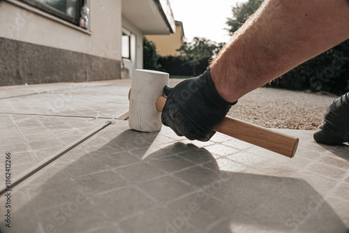 Terrace construction.Tile laying works.Laying Patio Tiles with Rubber Mallet.Person Installing Stone Pavers with Rubber Mallet. construction hammer taps tiles.Hands in black gloves lay tiles on a