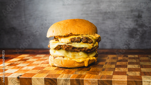 Tableau sur toile Massive triple deck smash burger with melted cheese dripping down, beautifully presented on a wooden board