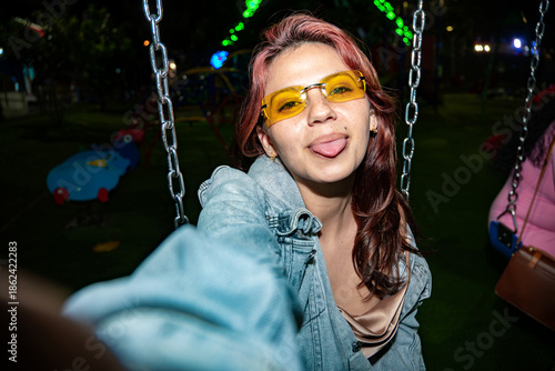 Woman posing on swing sticking tongue out at night