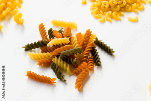 Uncooked Turkish colorful spiral pasta with tomatoes and spinach on white surface