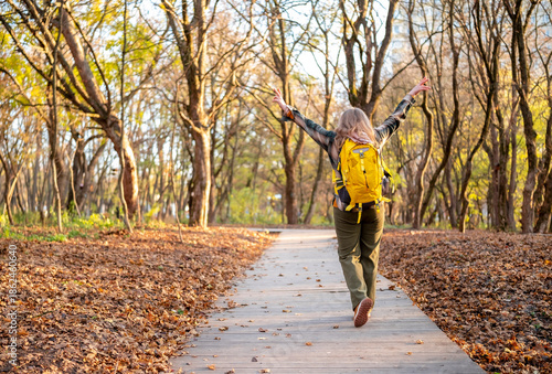 Obraz na plátně Blonde woman walking in autumn forest on narrow trail with yellow backpack and plaid shirt