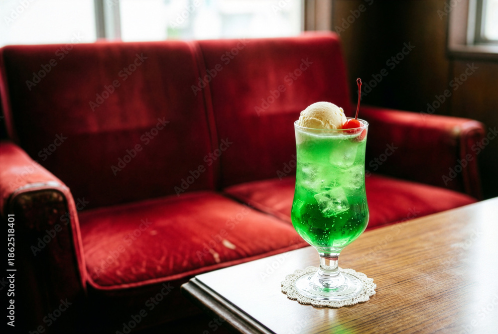 Fototapeta premium Retro style melon cream soda with ice cream and cherry on a wooden table in a nostalgic Japanese kissaten coffee shop with red velvet sofa background.